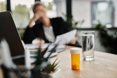 Téléchargez les photos : A woman, stressed and overwhelmed, sits at a desk with a bottle of medicine in front of her. - en image libre de droit