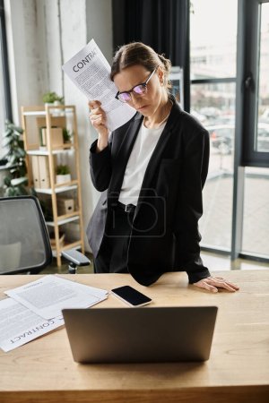 Stressed middle-aged woman in business suit sits at desk with papers.