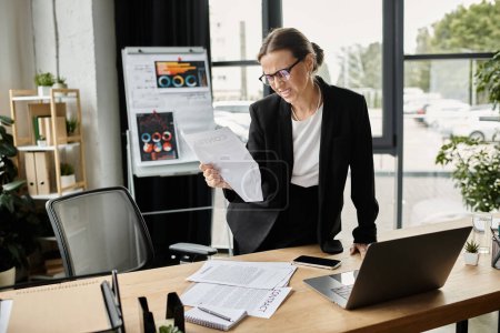 Téléchargez les photos : Middle-aged woman stressed at office desk with papers. - en image libre de droit