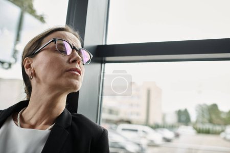 Foto de A middle-aged businesswoman in glasses gazes away, depression. - Imagen libre de derechos