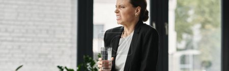 Woman holding glass of water in front of window.