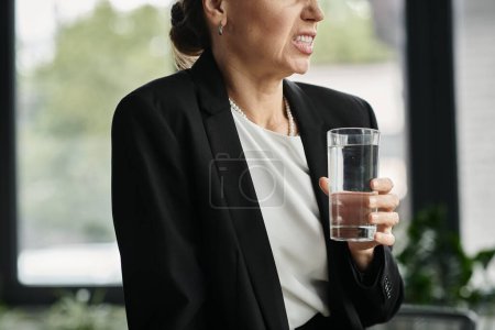 A businesswoman in her office holding a glass of water.
