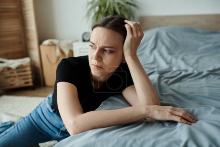 Middle-aged woman lying on bed with head in hands, showing signs of depression.