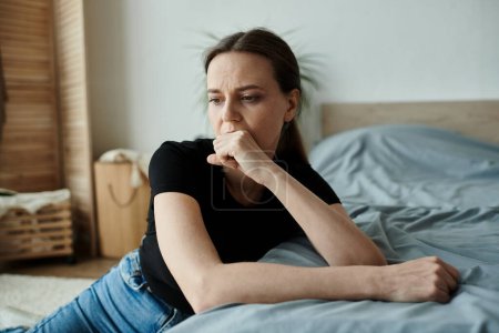 Woman in deep thought, resting on bed with chin on hand.