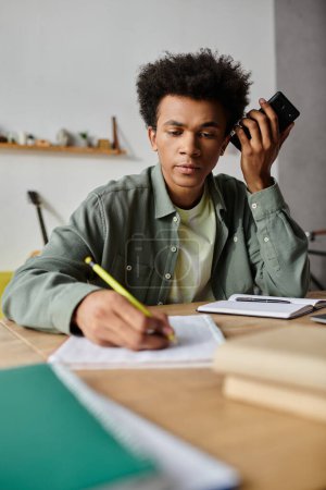 Young African American man sitting at desk, talking on phone.