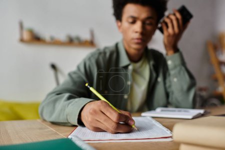 Foto de A young African American man sitting at a desk, writing in a notebook. - Imagen libre de derechos