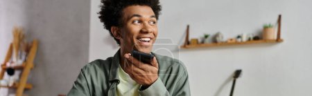 A young man smiles while holding a cell phone.