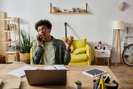 Téléchargez les photos : A young African American man talks on the phone while studying online at home. - en image libre de droit