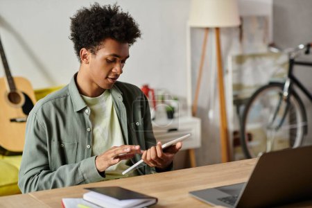 Téléchargez les photos : A young African American man studying online with a laptop and a tablet at a table. - en image libre de droit