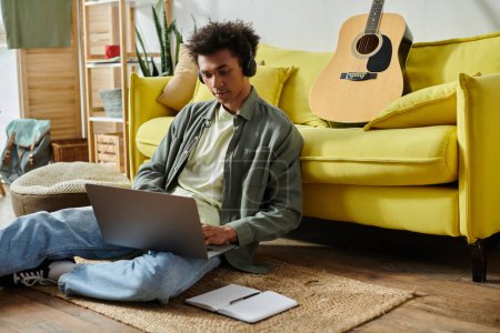 Young man with guitar and laptop on floor.