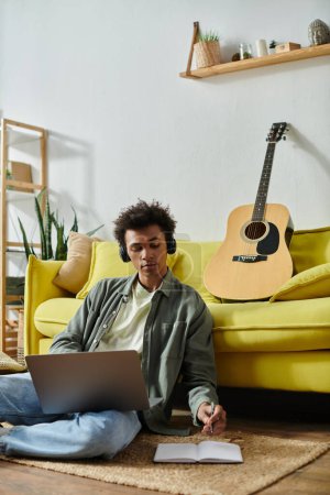 A young man, headphones on, strums a guitar on a yellow couch.