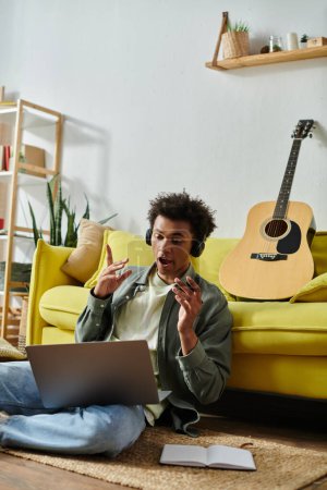 Young man creating music online with guitar and laptop.