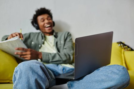Foto de Young man studying with laptop on yellow couch and headphones. - Imagen libre de derechos
