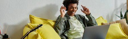 Téléchargez les photos : Young man, African American, sitting on yellow couch, using laptop for online study. - en image libre de droit
