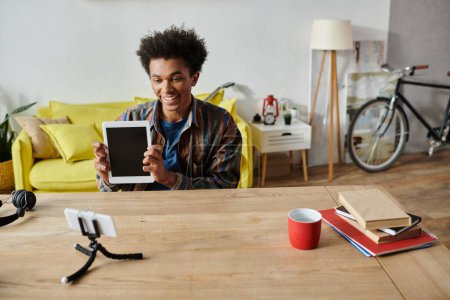 Young man, African American, holding tablet, in front of yellow table.