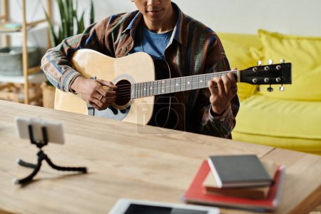 Téléchargez les photos : A young African American man passionately playing an acoustic guitar at home. - en image libre de droit