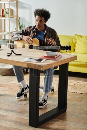 Young man creates music with acoustic guitar on rustic table.