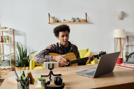 A young man playing acoustic guitar in front of a phone, recording for his blog.