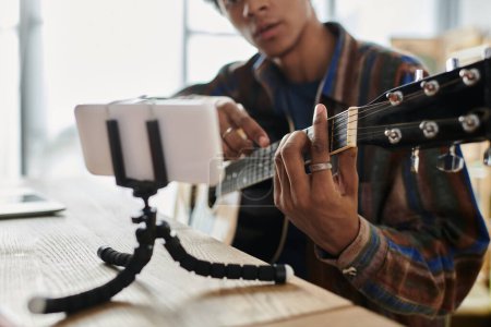 Photo for Man plays guitar in front of phone while recording a vlog. - Royalty Free Image