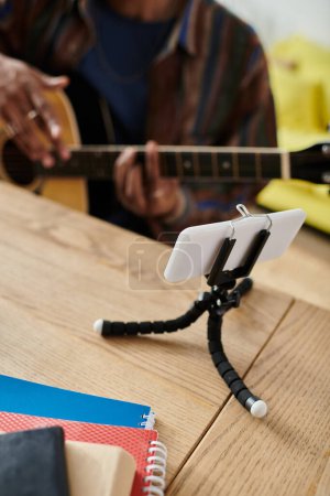 A man serenading with guitar, cell phone on table.