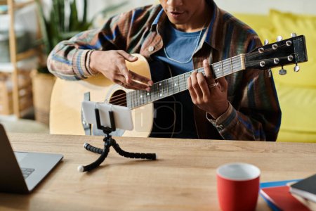 Young African American male blogger plays guitar while speaking on phone camera.