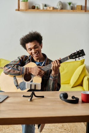 A man strums an acoustic guitar in front of a phone, creating music for an online audience.
