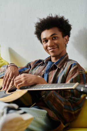 Young man strums acoustic guitar on yellow couch.