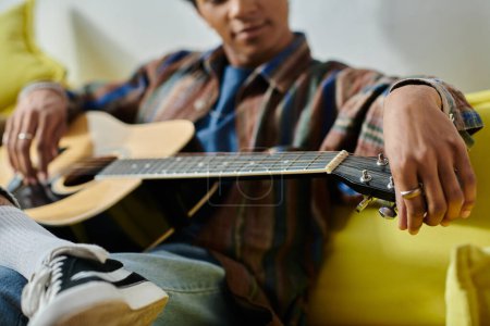 Young man serenades with acoustic guitar on cozy yellow couch.