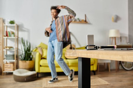 Foto de A young African American male blogger stands in a living room, working on a phone while talking on his phone camera. - Imagen libre de derechos