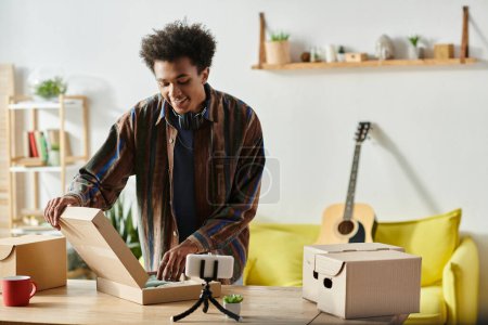 A young African American male blogger opens a box in his living room while talking on the phone camera.