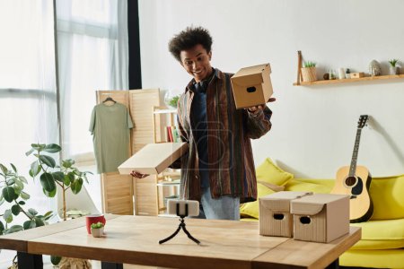 Foto de Young African American man holding cardboard box while vlogging in living room. - Imagen libre de derechos