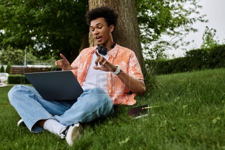 Téléchargez les photos : Young man using laptop while seated on grass - en image libre de droit