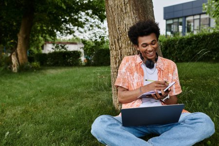 Young man sitting on grass with headphones and laptop.