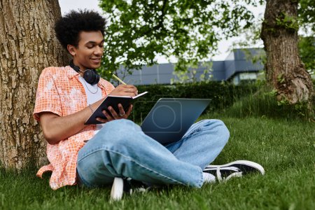 Black man working on laptop in grassy park setting.