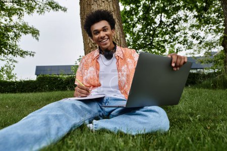 Photo for A young African American man sitting on grass with a laptop in a park. - Royalty Free Image