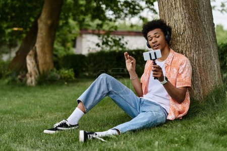 Téléchargez les photos : Young man sitting on grass, engrossed in cell phone. - en image libre de droit