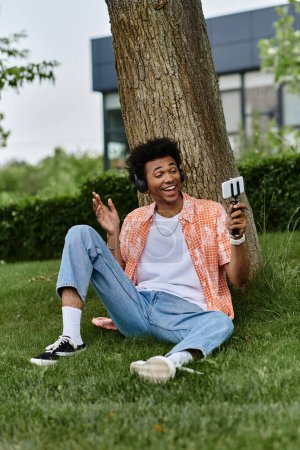 Téléchargez les photos : A young man of African descent sits on grass beside a tree. - en image libre de droit