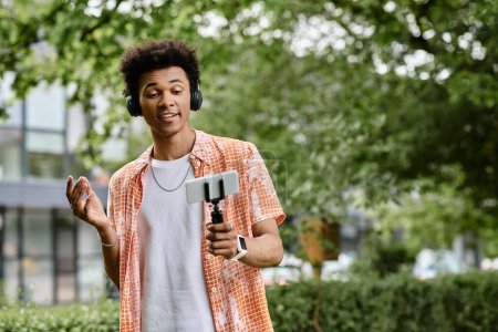 Téléchargez les photos : A young african american man enjoys the tranquility of a park while holding a cell phone. - en image libre de droit
