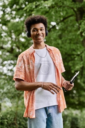 Young man in headphones listening to music, standing in a park.
