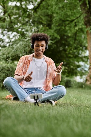 Young African American man sitting on grass, pointing at his phone.
