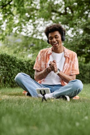 A young man of African American descent sitting on the grass, immersed in music.