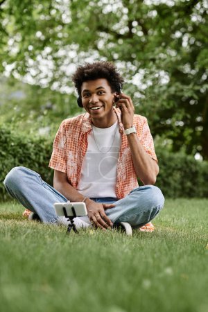 Young man, African American, sitting on grass, listening to music on phone.