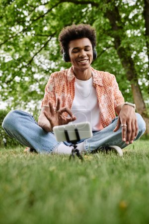 Téléchargez les photos : Young man immersed in music sits on grass in park with headphones on. - en image libre de droit
