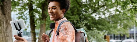 Photo for Young African American man, backpack on, using cell phone in the park. - Royalty Free Image