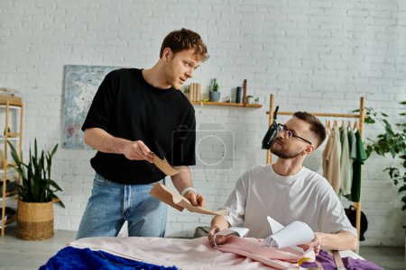 Dos hombres, una pareja gay, trabajan juntos en un taller de diseño cortando un trozo de papel para su atuendo de moda.
