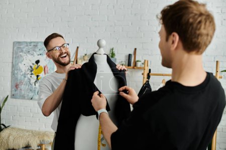 A man and mannequin hold a black shirt, working in a designer workshop.