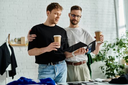 Foto de Dos hombres, parte de un elegante dúo de diseño, disfrutan de una pausa para tomar un café juntos, sosteniendo tazas y charlando. - Imagen libre de derechos