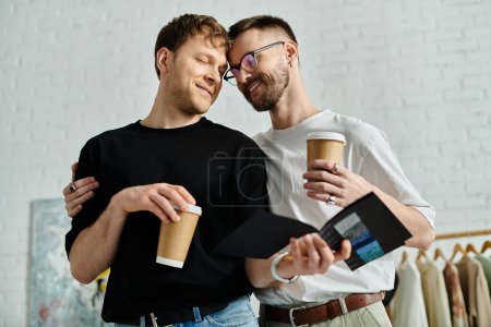 Foto de Dos hombres, parte de una pareja gay, se mantienen unidos mientras confeccionan ropa elegante en su taller de diseño. - Imagen libre de derechos