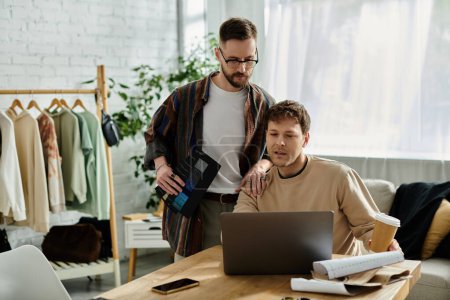 Zwei Männer, Partner im Design, diskutieren bei einem Laptop in einem stylischen Bekleidungsgeschäft über Ideen.