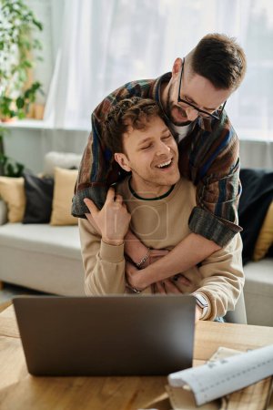 A man embraces his partner as the latter works on a laptop in a trendy designer workshop.